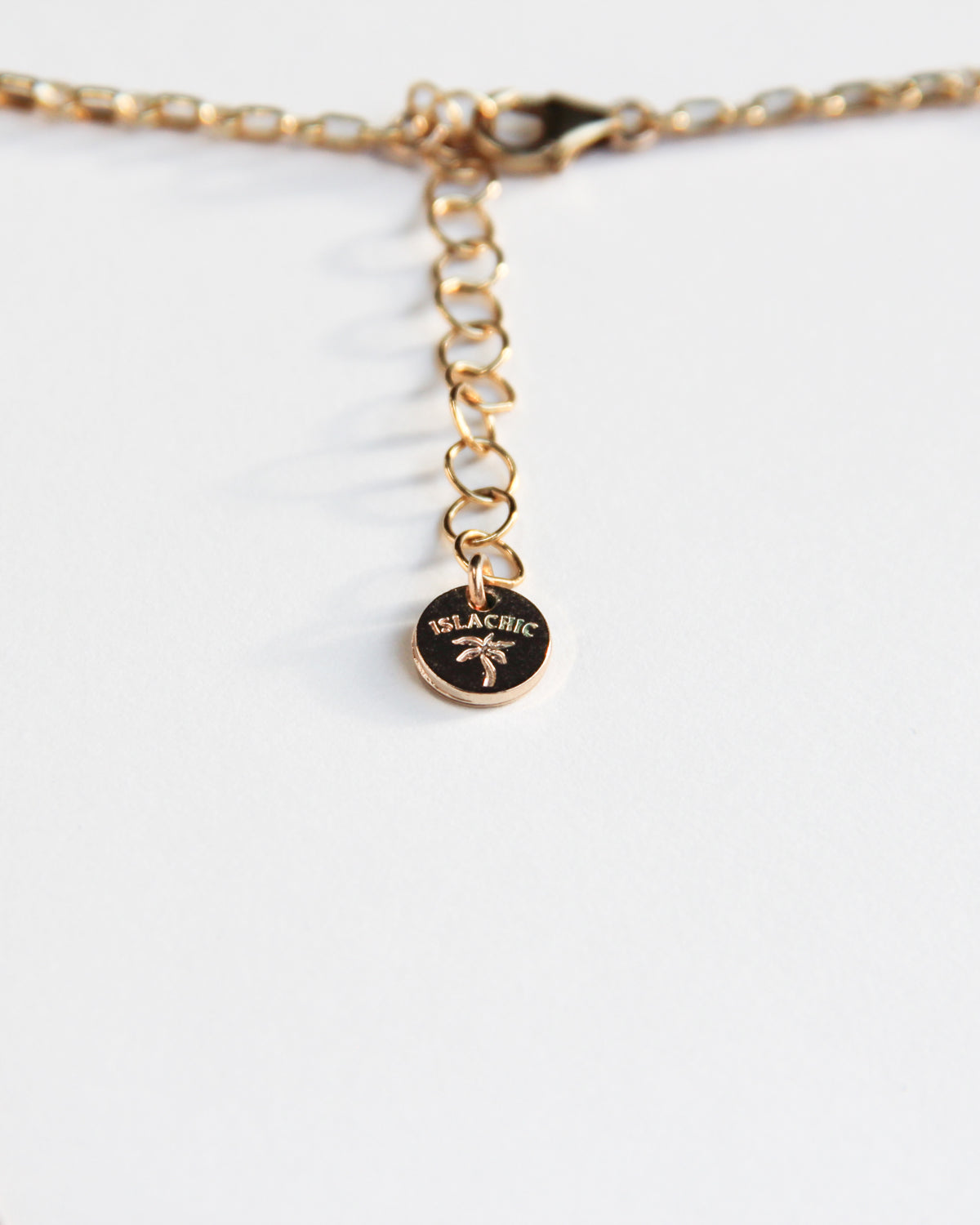 Close-up of islachic gold branding tag for gold-filled multi-charm necklace with heart, seashell, pearl, sun, blue gemstone, and watermelon charms on a delicate gold chain.