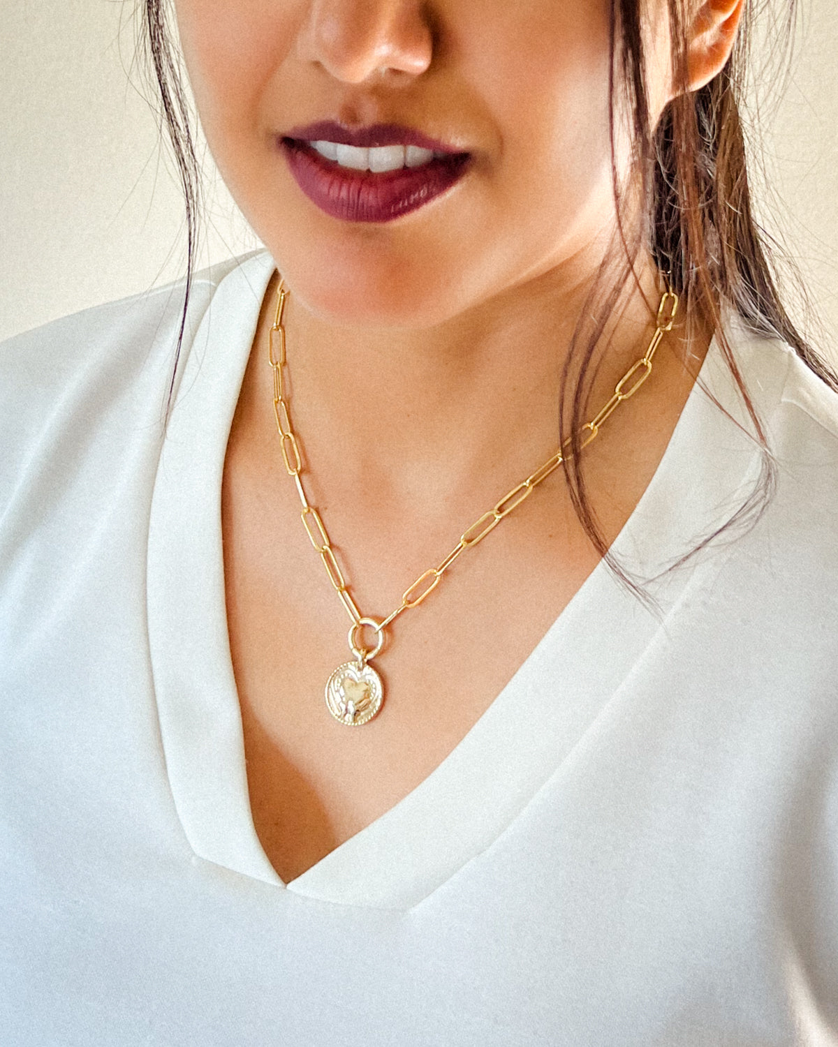 Gold-paperclip necklace with a circle pendant featuring a hand and heart design.