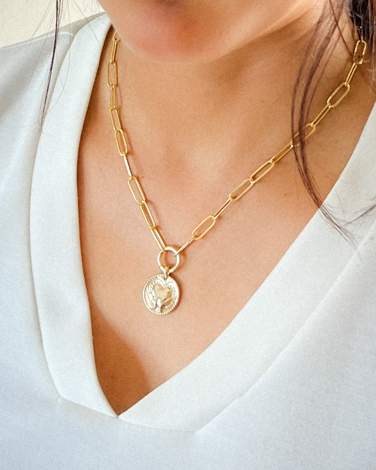 Gold-paperclip necklace with a circle pendant featuring a hand and heart design.