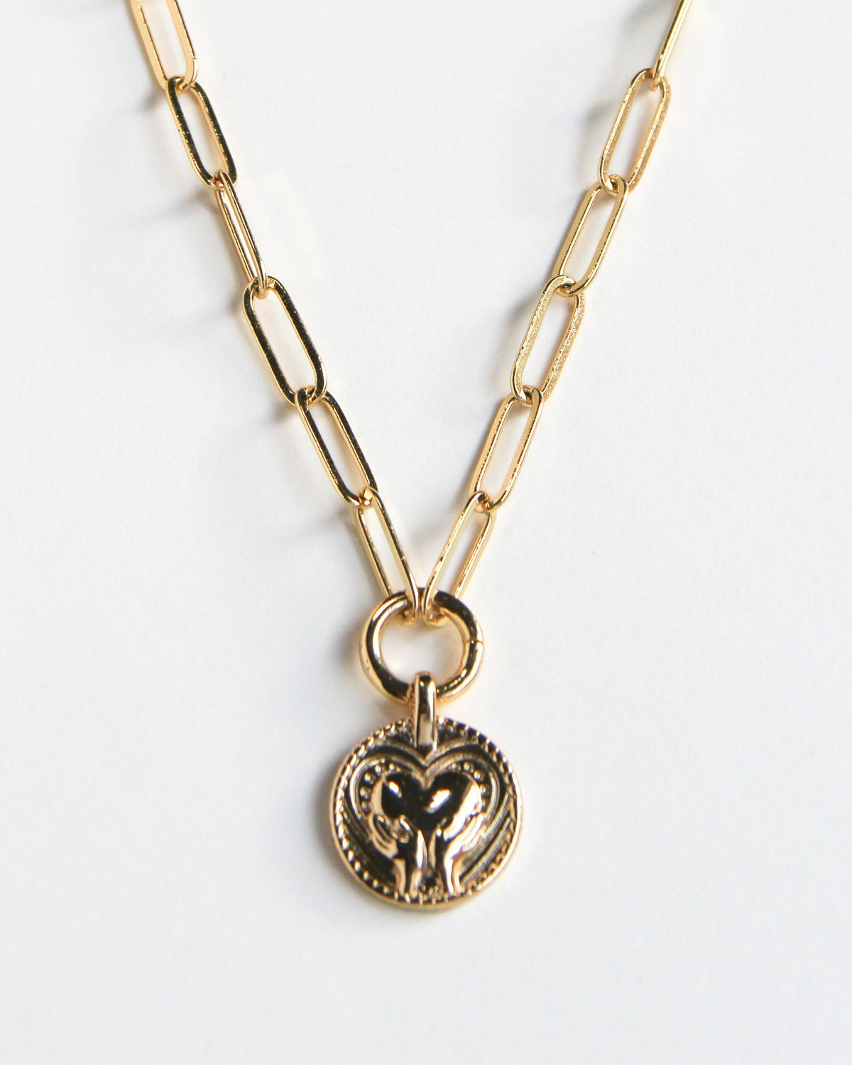 Gold-paperclip necklace with a circle pendant featuring a hand and heart design.