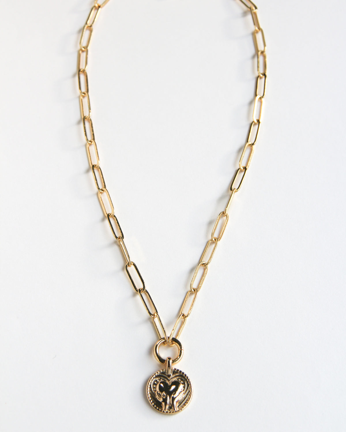 Gold-paperclip necklace with a circle pendant featuring a hand and heart design.