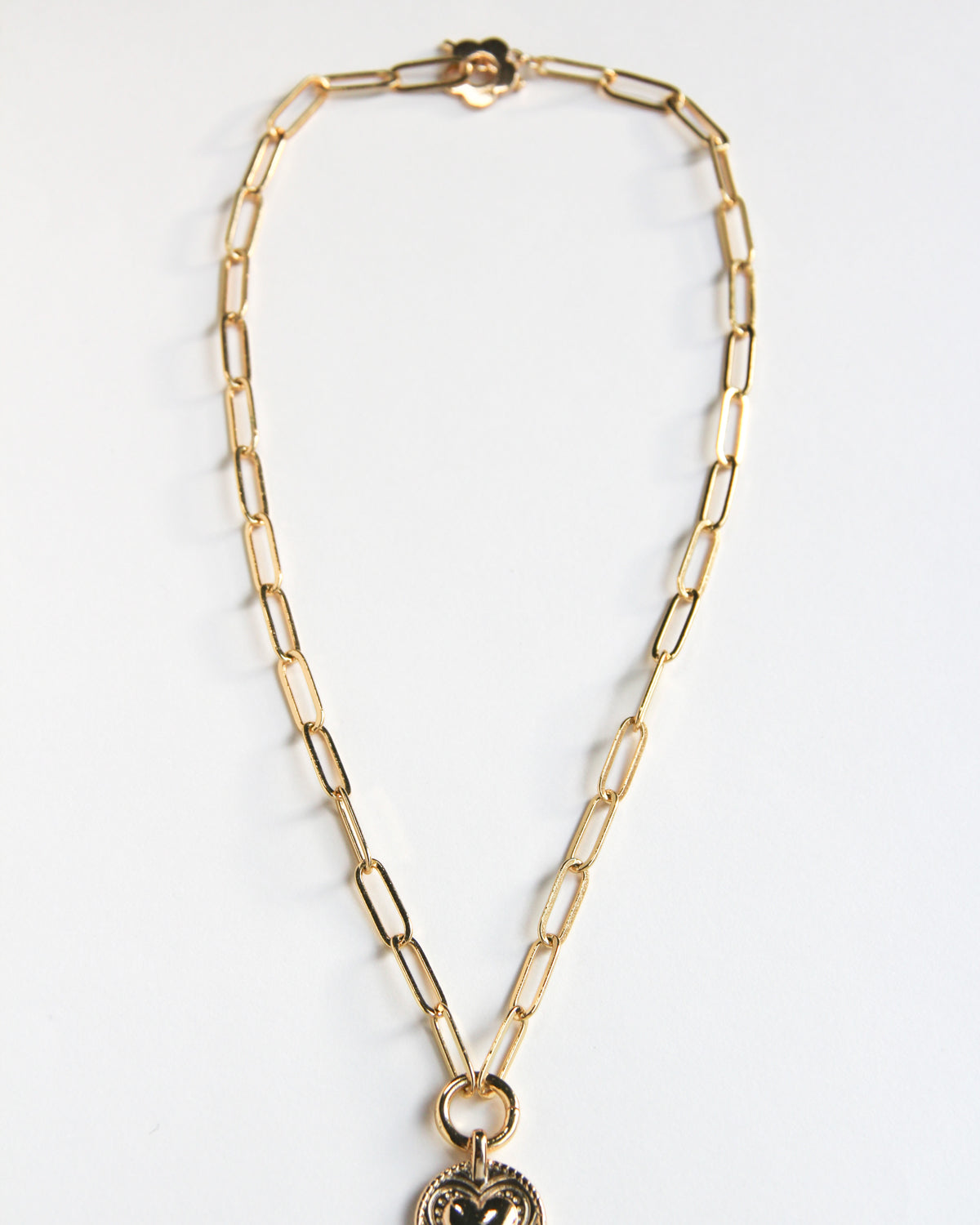 Gold-paperclip necklace with a circle pendant featuring a hand and heart design.