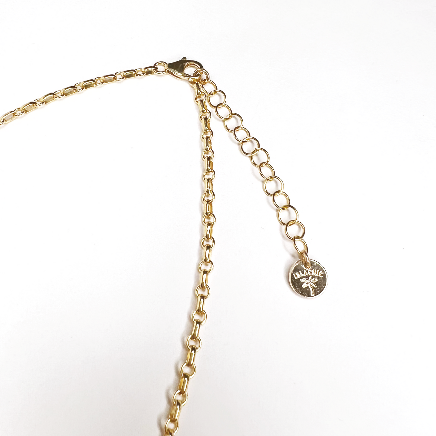 A close-up image of an extender chain with IslaChic branding tag on a 3 charm gold-filled necklace on a white surface. Necklace can be adjustable from 16 inches to 18 inches. Necklace has a star, body, and a cubic zirconia heart charm.