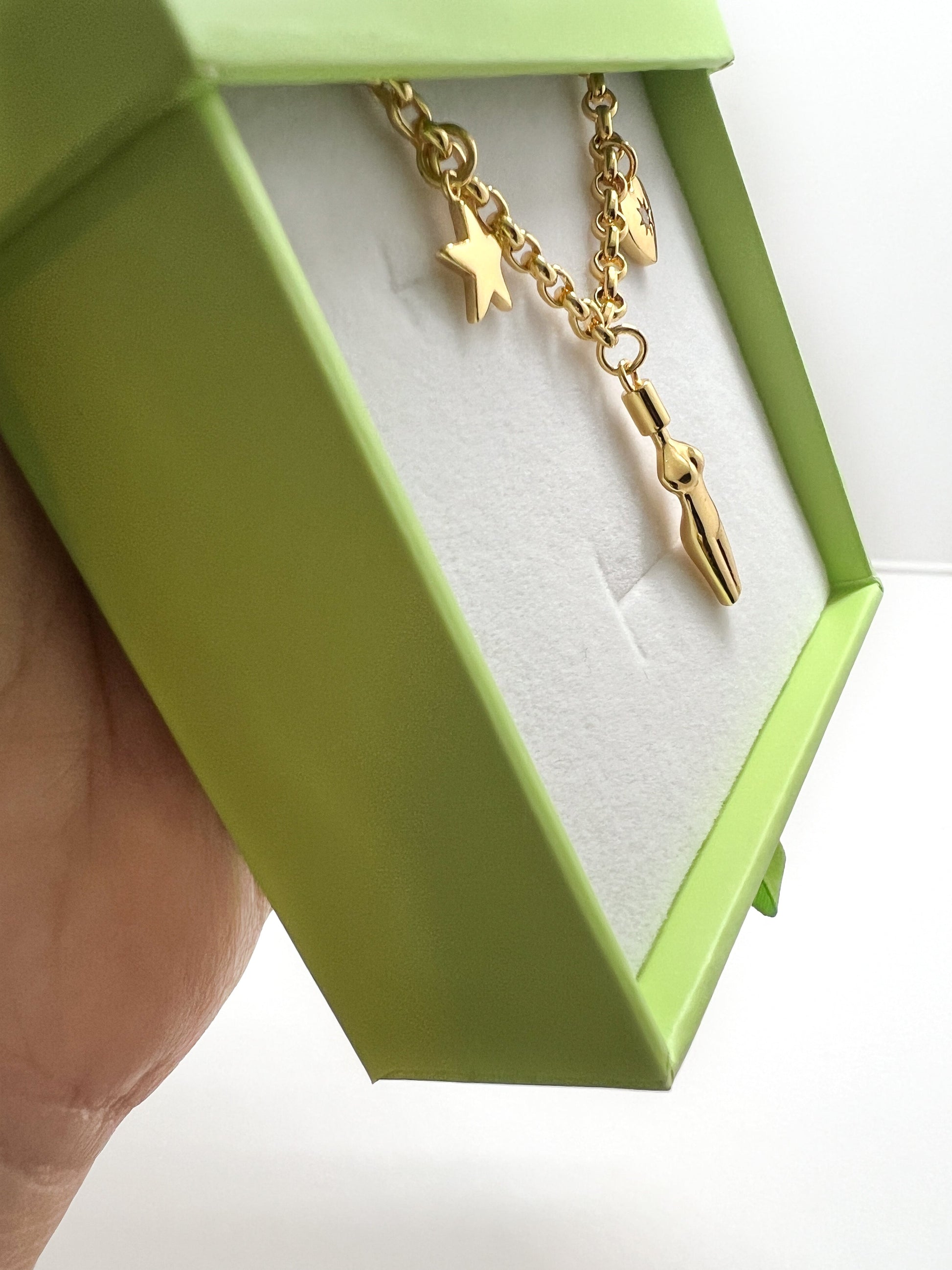 Angled view of the gold Lucia Charm Necklace, showing the side profiles and 3D detail of the heart, goddess, and star charms in a green IslaChic box.