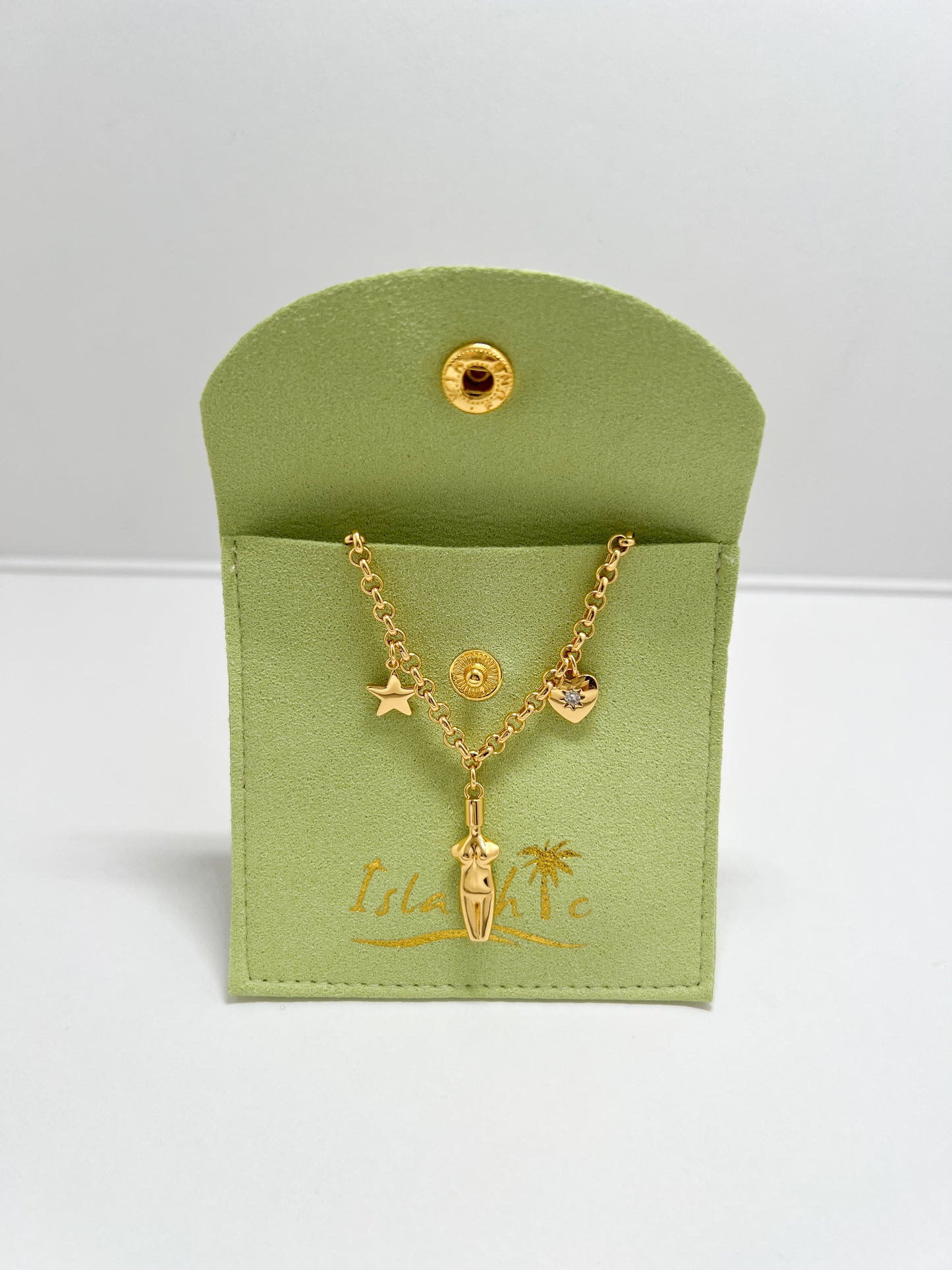 The Lucia Charm Necklace draped over a matching lime green fabric jewelry pouch with a gold snap closure and embossed IslaChic logo