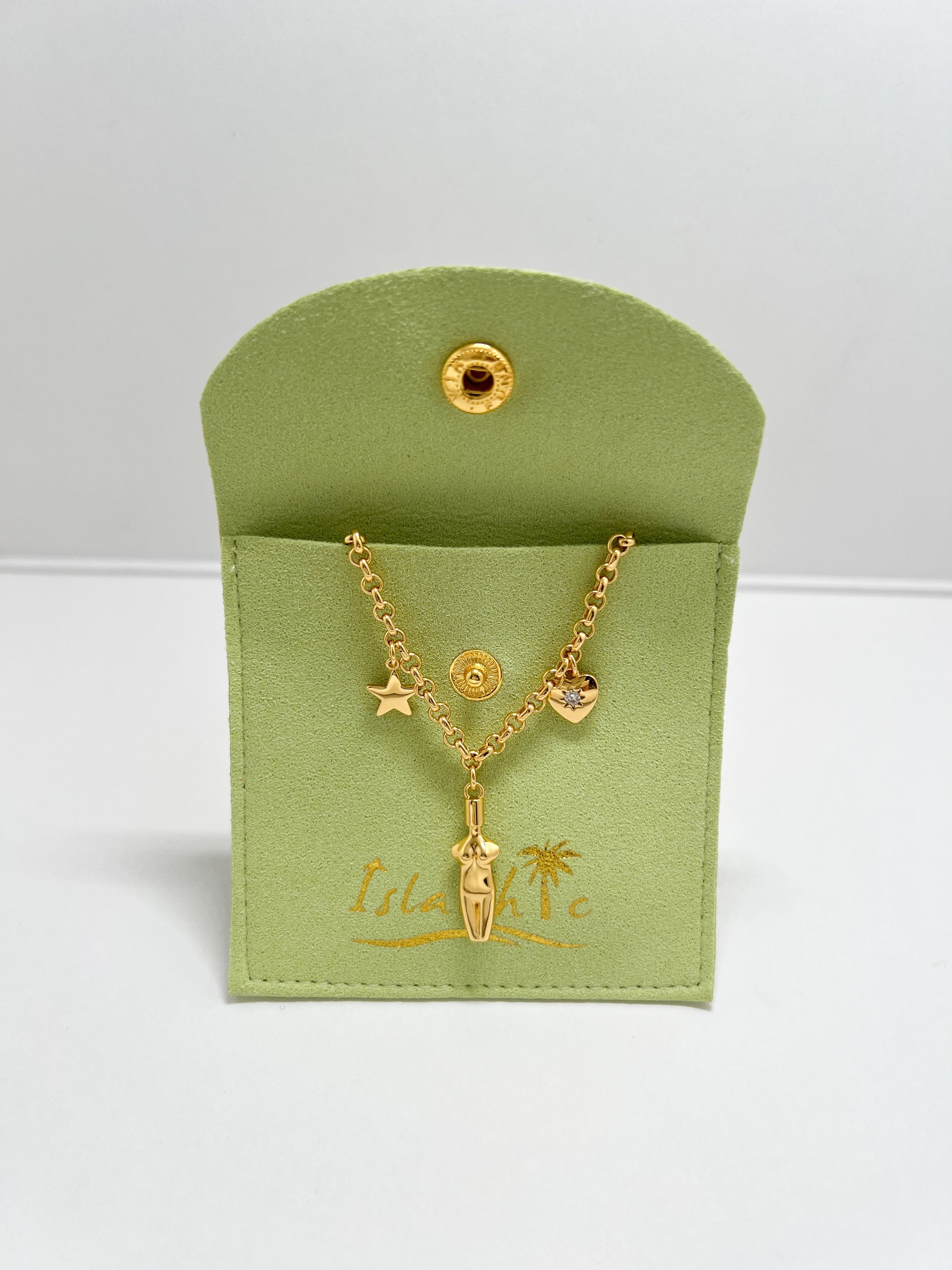 The Lucia Charm Necklace draped over a matching lime green fabric jewelry pouch with a gold snap closure and embossed IslaChic logo