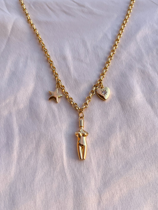 A top-down view of the Lucia Charm Necklace resting on soft white textured fabric, highlighting the intricate chain links and polished charms, star, body, and heart.