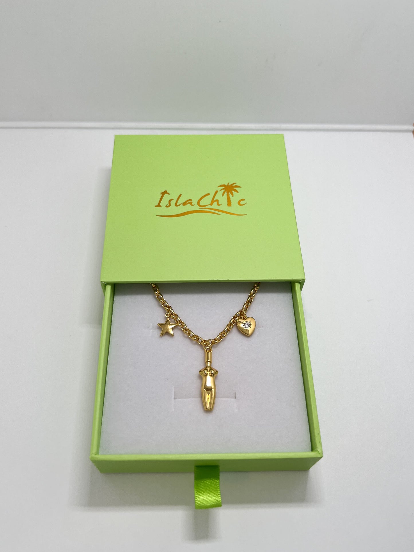 The Lucia Charm Necklace displayed inside an open lime green IslaChic gift box on a white velvet interior cushion.