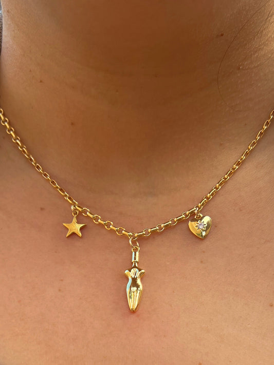 A close-up of model’s neck and chest area wearing the Lucia charm necklace worn.  A 3 charm gold-filled necklace with a star (left side), body (center charm), and a cubic zirconia heart charm (right side). Heart charm has a cubic zirconia stone setting in the center of charm.